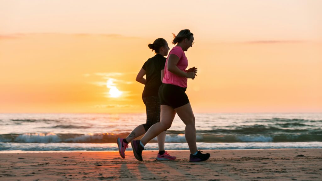 Two women running on a beach for a healthy living.